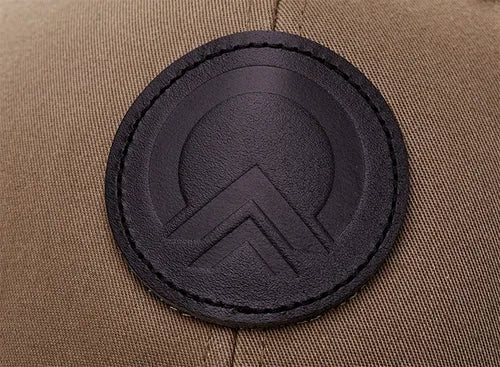 Round tonal black debossed leather patch on an olive cap